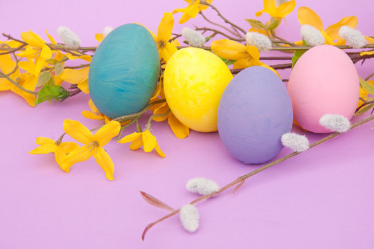 Closeup image of hand painted Easter eggs with Forsythia flowers and pussy willows against purple background