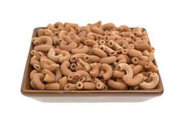 Red rice pasta elbows in a brown square dish isolated on a white background.