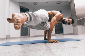 Athletic strong man practicing difficult yoga pose.