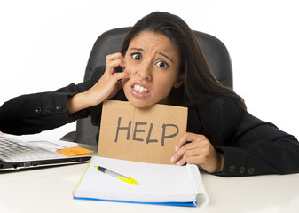 young busy desperate Latin businesswoman holding help sign sitting at office desk in stress worried