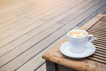 coffee cup on a wooden table in a coffee shop outdoors. enough space for copy, lettering and text. graded with a flare.

