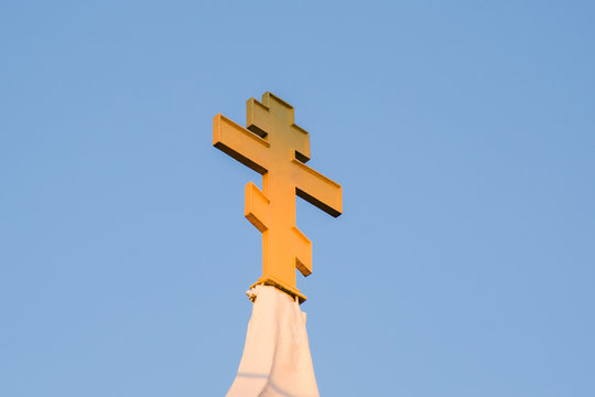 The sunset light shines on the iron cross Orthodox church tower apex. Blue sky background.