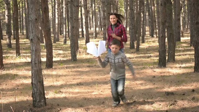 Boy running with a paper airplane and it catches up with his mom. Slow motion. Little boy playing paper airplane with his mother in wood.