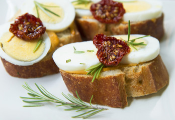 Small sandwiches with boiled eggs, dried tomatoes and rosemary