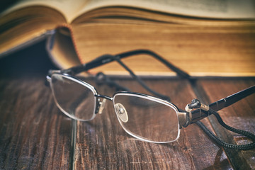 Reading glasses in front of old yellow book on rustic wooden background