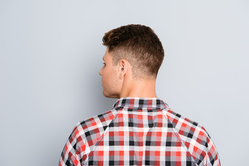 Back view of young guy in chekered shirt  on gray background