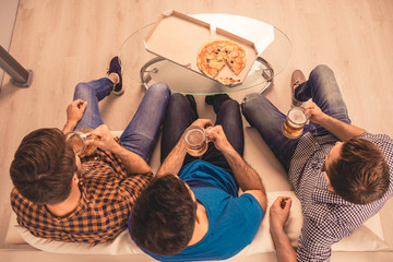 Top view of three friends sitting on sofa with beer and pizza