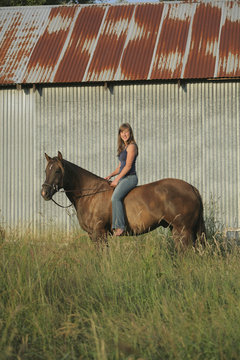 A Girl Sitting On A Horse In Front Of A Metal Barn; Troutdale, Oregon, United States of America