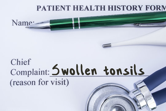 Complaint of swollen tonsils. Paper health history form, which is written on patient's chief complaint of swollen tonsils, surrounded by a stethoscope, electronic thermometer and green ball-point pen 