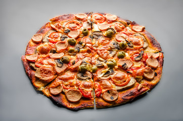 Pizza with mushrooms, olives, mozzarella, tomatoes and sausages on black background