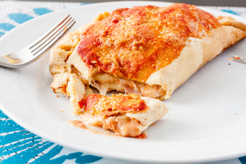 A cut open calzone, a type of folded pizza, showing the melted oozing cheese on a white plate