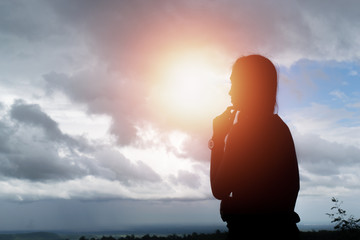 Silhouette of woman praying over beautiful sky background.