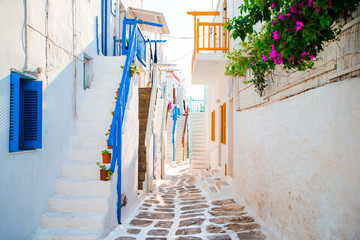 The narrow streets of greek island with blue balconies, stairs and flowers. Beautiful architecture building exterior with cycladic style.