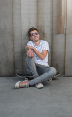 Young stylish man in sunglasses sitting on a skateboard.