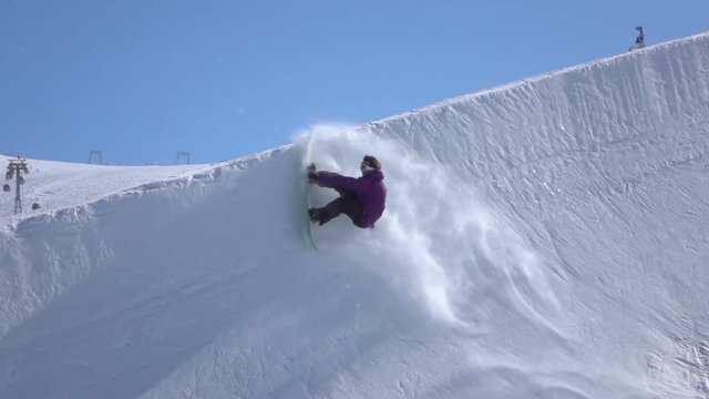 SLOW MOTION: Young pro snowboarder spraying snow in half pipe in sunny snowpark