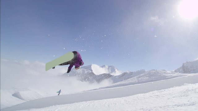 SLOW MOTION: Young pro snowboarder jumping over the sun in half pipe snow park