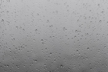 Photo of raindrops on window glasses surface with cloudy background.