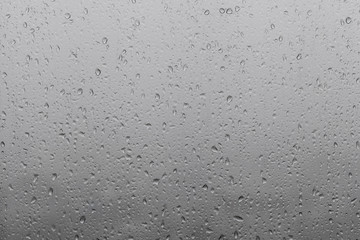 Photo of raindrops on window glasses surface with cloudy background.