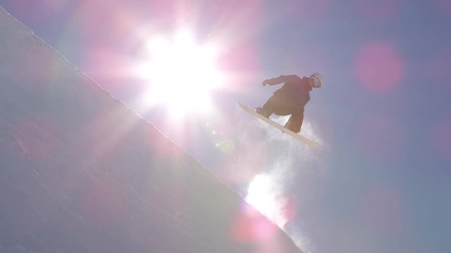 SLOW MOTION: Young pro snowboarder jumping over the sun in half pipe snow park