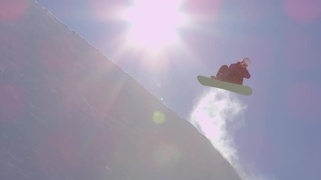 SLOW MOTION: Young pro snowboarder jumping over the sun in half pipe snow park