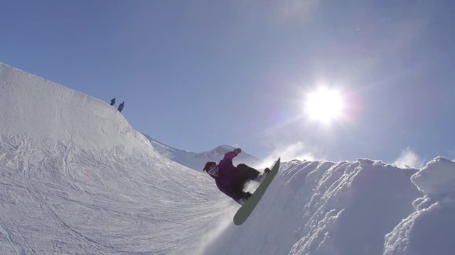 SLOW MOTION: Young pro snowboarder spraying snow in half pipe in sunny snowpark
