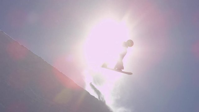 SLOW MOTION: Young pro snowboarder jumping over the sun in half pipe snow park