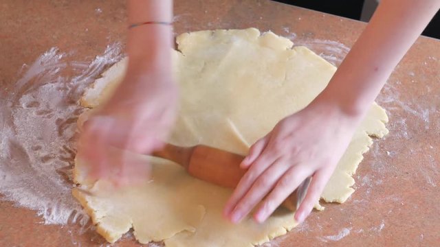 Baker kneading dough with rolling pin on table prepares bread or apple pie