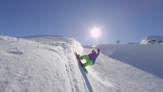 SLOW MOTION: Young snowboarder spraying snowflakes in halfpipe in sunny snowpark