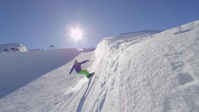 SLOW MOTION: Young pro snowboarder sliding on half pipe wall, spraying snow
