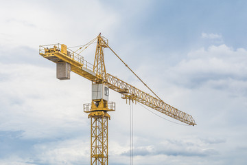 Yellow iron crane standing against the blue cloudy sky.