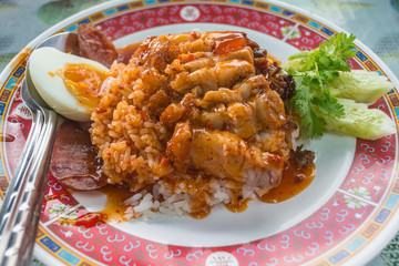 Crispy pork rice with egg and delicious sauce in a red dish.