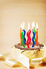 Birthday cake with many decorative burning candles against beige background
