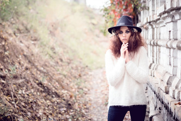 Beautiful girl on brick wall background. Girl in the hat. Gloomy makeup. Halloween. Fashionable woman. Casual wear. Trend clothing. Toned image.
