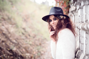 Beautiful girl on brick wall background. Girl in the hat. Gloomy makeup. Halloween. Fashionable woman. Casual wear. Trend clothing. Toned image.