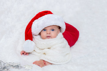 Baby girl on the bed wearing a Santa hat for Christmas.