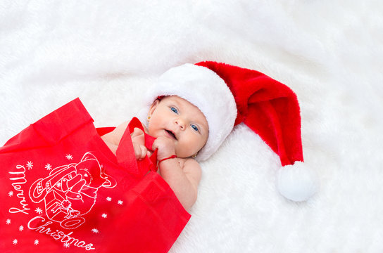 Cute baby girl on the bed wearing a Santa hat for Christmas.