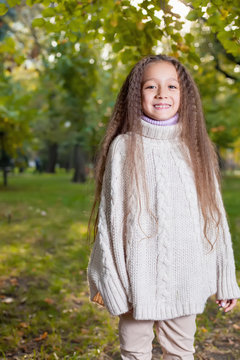 Beautiful little girl in white sweater posing in autumn Park nea