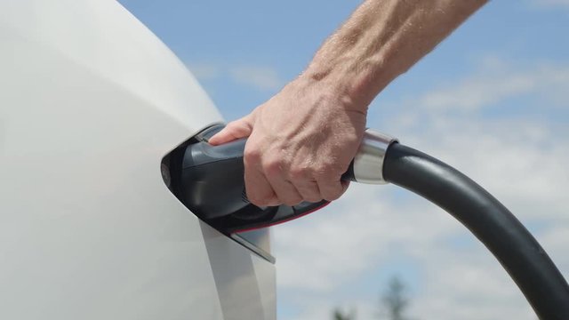 CLOSE UP: Caucasian man unplugging Tesla car from electricity grid  on sunny day