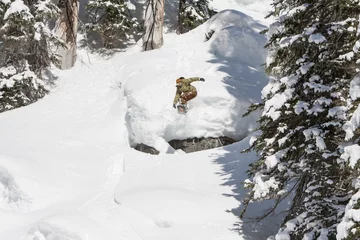 Fotobehang Wintersport Snowboarding Man Jump off Cliff in Sunny Powder Snow  © CascadeCreatives