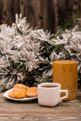 Cup of coffee, cookies, candle, fir branch in snow on wooden background