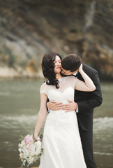 Elegant stylish happy brunette bride and gorgeous groom on the background of a beautiful waterfall in the mountains
