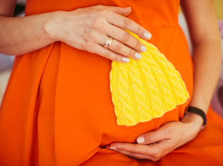 Pregnant lady in orange dress holds yellow child's hat before he