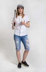 Young attractive woman with a baseball bat and ball. Cool girl in ragged shorts, shirt and a baseball cap. A girl holding a bat on his shoulder.