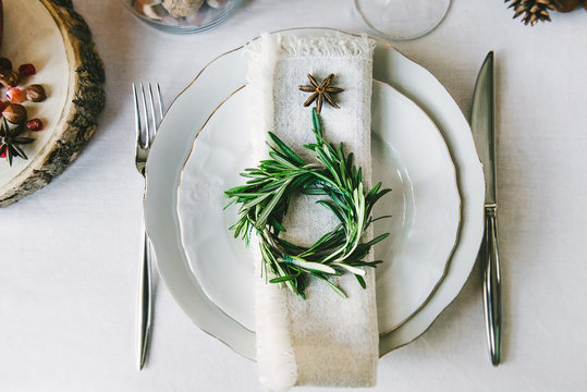 Decorative green wreath on a napkin as a part of table appointments , clean white tablecloth background, top view. Christmas table place setting.