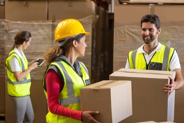 Smiling warehouse workers carrying a cardboard box