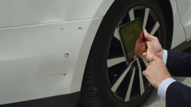 CLOSE UP: Insurance agent estimating damages on Tesla Model S with tablet 