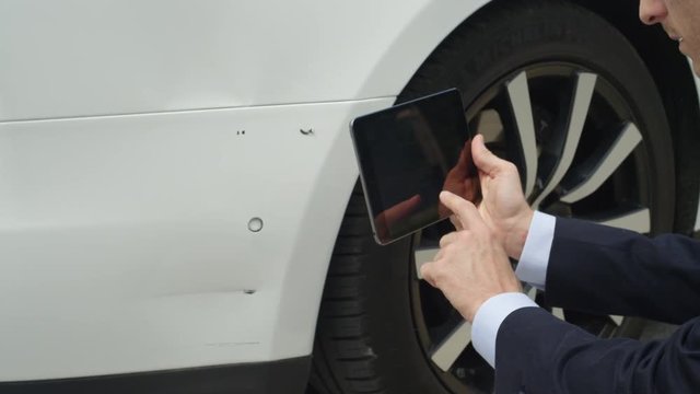 CLOSE UP: Insurance inspector estimating damages on Tesla Model S with tablet 