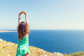 girl with green dress stretching her arms raised looking at ocea