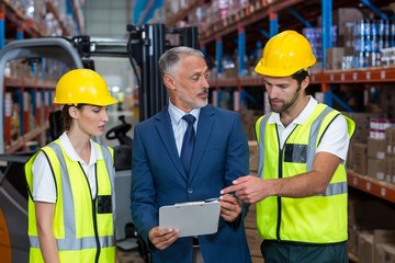 Warehouse manager and co-workers discussing over clipboard