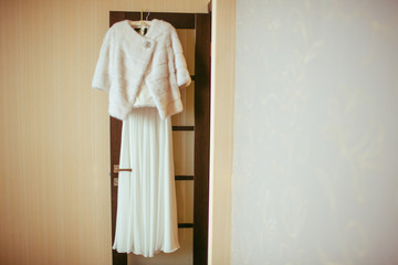 White fur coat hangs over a wedding gown on the door